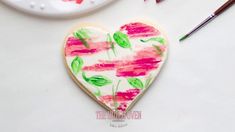 a heart shaped cookie decorated with pink and green flowers next to crayon markers