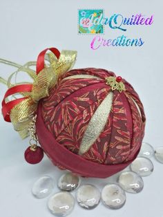 a red ornament sitting on top of some glass beads with a gold ribbon around it