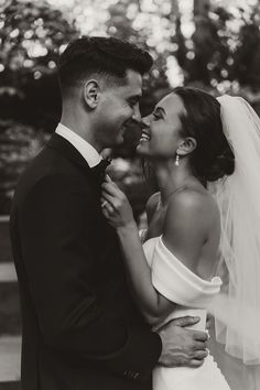 black and white photo of bride and groom smiling at each other with trees in the background