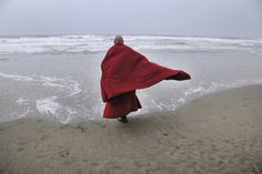 a man in a red robe is walking on the beach