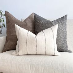 three pillows on a couch with a plant in the corner