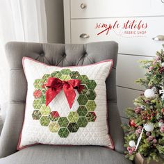 a christmas wreath pillow sitting on top of a gray chair next to a christmas tree