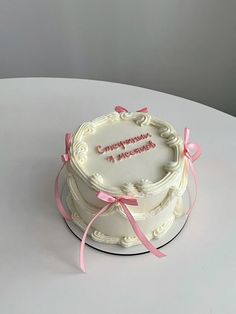 a white cake with pink ribbon and congratulations message on top, sitting on a table