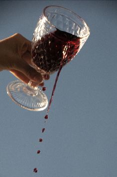 a person pouring red liquid into a wine glass on top of a blue sky background