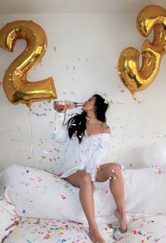 a woman sitting on a bed with balloons and confetti