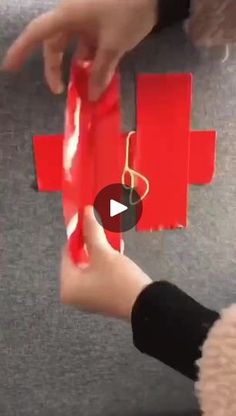 someone is holding a red piece of paper with scissors in it and another person's hand