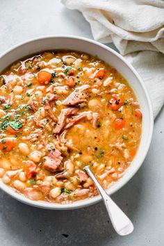 a white bowl filled with chicken and bean soup on top of a table next to a napkin