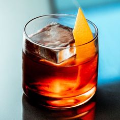 a close up of a drink with an orange peel on the top and ice cubes in it