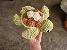 a hand holding a small stuffed animal in the shape of a turtle