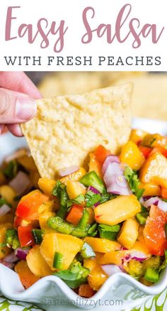 a hand dipping a tortilla chip into a bowl filled with fresh fruit salsa