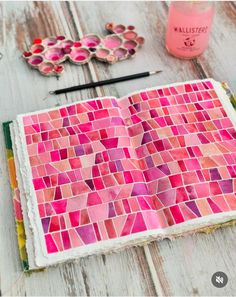 an open book with pink and red mosaic tiles on it next to paintbrushes