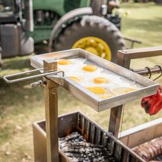 an outdoor grill with eggs and sausages cooking on it's griddle in front of a tractor