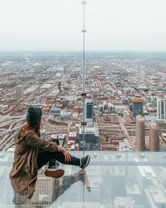 a man sitting on top of a tall building next to a cityscape with buildings in the background