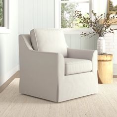 a white chair sitting in front of a window next to a vase filled with flowers