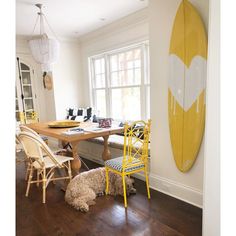 a dog sitting in front of a wooden table with chairs and a surfboard on the wall