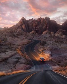 a truck is driving down the road in front of some rocks and mountains at sunset