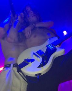 a shirtless man laying on top of a white guitar