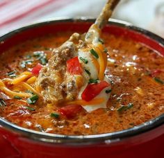 a spoon full of soup with meat and cheese on top, in a red bowl