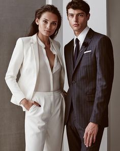 a man in a suit and woman in a white jumpsuit posing for the camera