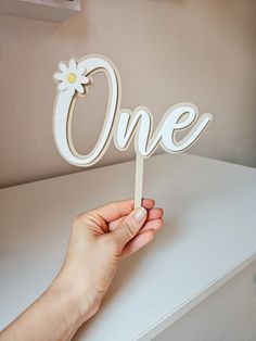 a person holding up a one sign on top of a white table with a flower