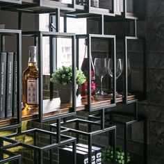 a shelf with wine glasses and bottles on it in front of a window filled with books