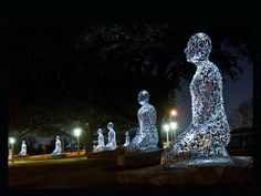 a group of statues sitting in the middle of a park at night with lights shining on them