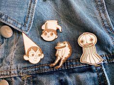 three pins with cartoon characters on them in the back pocket of a jean jacket,