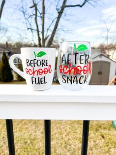 two coffee mugs sitting on top of a white fence next to each other in front of a house