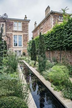 an old brick building is next to a small pond in the middle of a garden