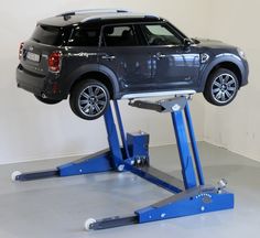 a car is on top of a lift in a room with concrete flooring and white walls