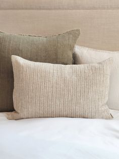 three pillows on top of a bed with white sheets and linens in the background