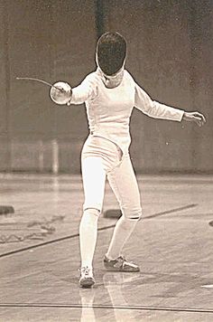 an old black and white photo of a woman in fencing gear holding a tennis racket