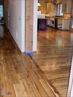 an empty living room and kitchen with wood flooring in the middle, looking out into the dining area