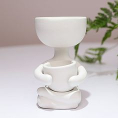 a white vase sitting on top of a table next to a green leafy plant