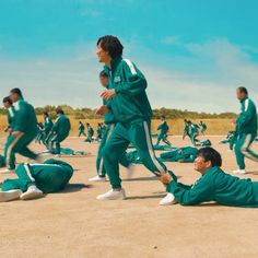 a group of men in green tracksuits are on the ground and one man is stretching