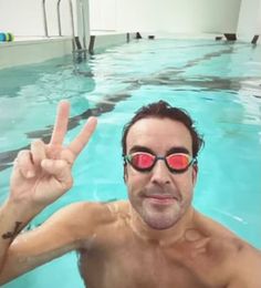 a man wearing sunglasses making the peace sign in a swimming pool