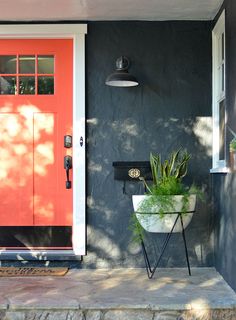 a planter with plants in it sitting on the front porch next to a red door