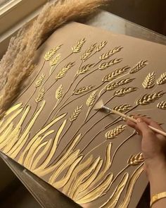 a person is using a brush to paint gold leaves on a piece of art paper