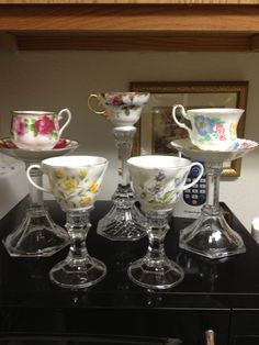 four glass cups and saucers sitting on top of a black table next to a mirror