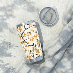 an orange and white floral print tumbler cup next to a drink can on a blanket