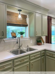 a kitchen with green cabinets and white counter tops, along with a window over the sink