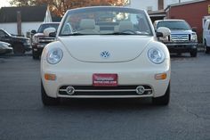 the front end of a white car parked in a parking lot next to other cars