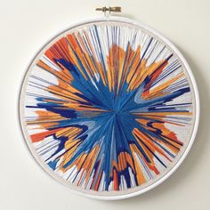 a blue and orange art piece on a white wall hanging from a hoop with scissors