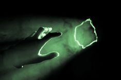 a hand holding something in the dark with green light coming from it's fingers