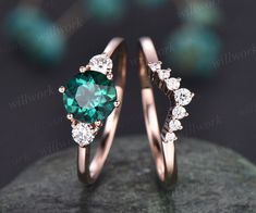 two wedding rings with green and white diamonds on top of each other, sitting on a rock