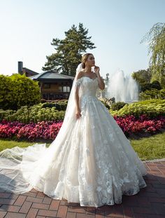 a woman in a wedding dress standing on a brick walkway next to flowers and trees