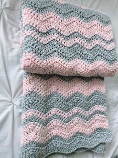 a crocheted blanket laying on top of a bed next to a white pillow