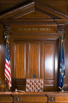 an executive desk with two american flags on the wall and in god we trust sign above it