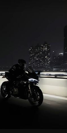 a man riding on the back of a motorcycle down a highway at night with city lights in the background