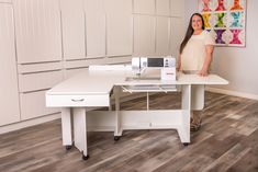 a woman standing next to a table with a sewing machine on it in front of her